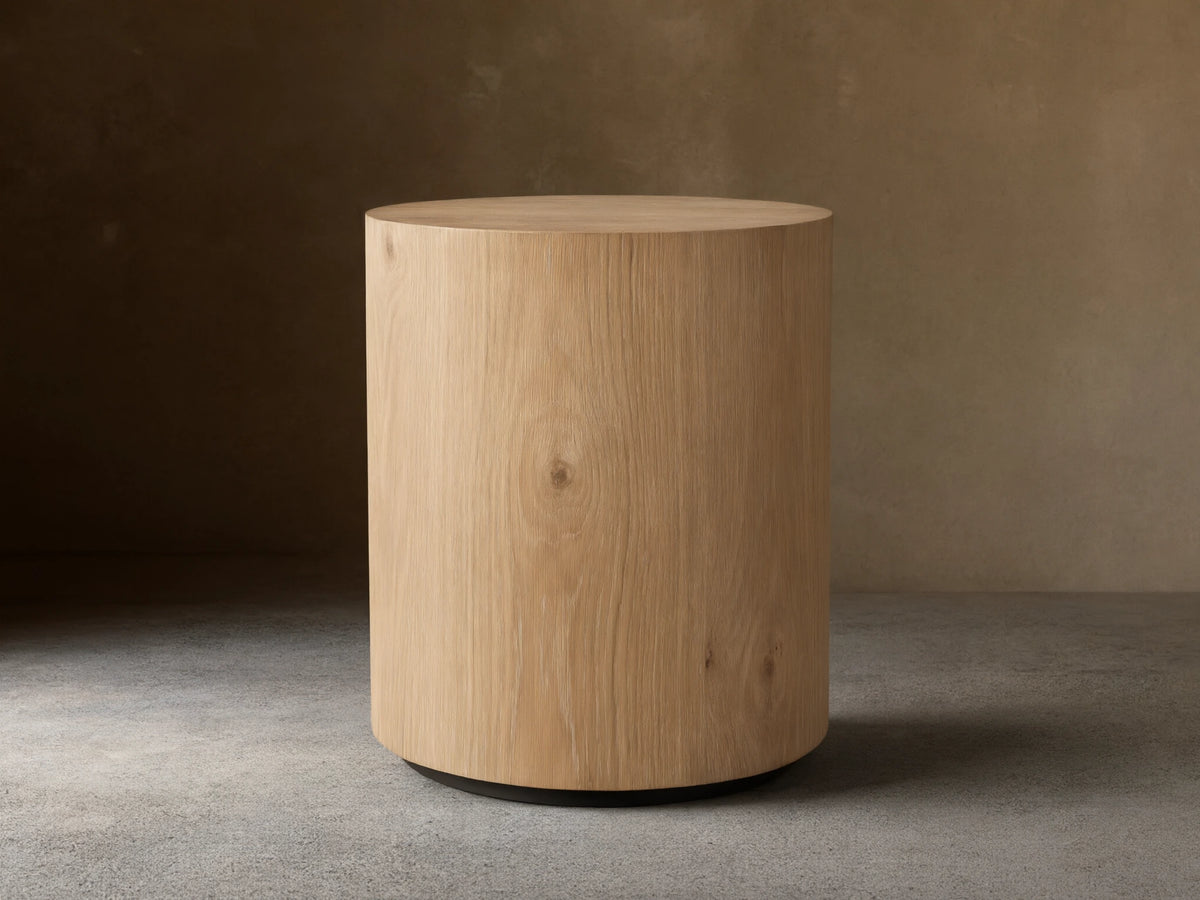 Sullivan Round End Table made of solid oak with a natural grain finish, cylindrical shape, on a black plinth-style base.
