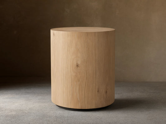 Sullivan Round End Table made of solid oak with a natural grain finish, cylindrical shape, on a black plinth-style base.