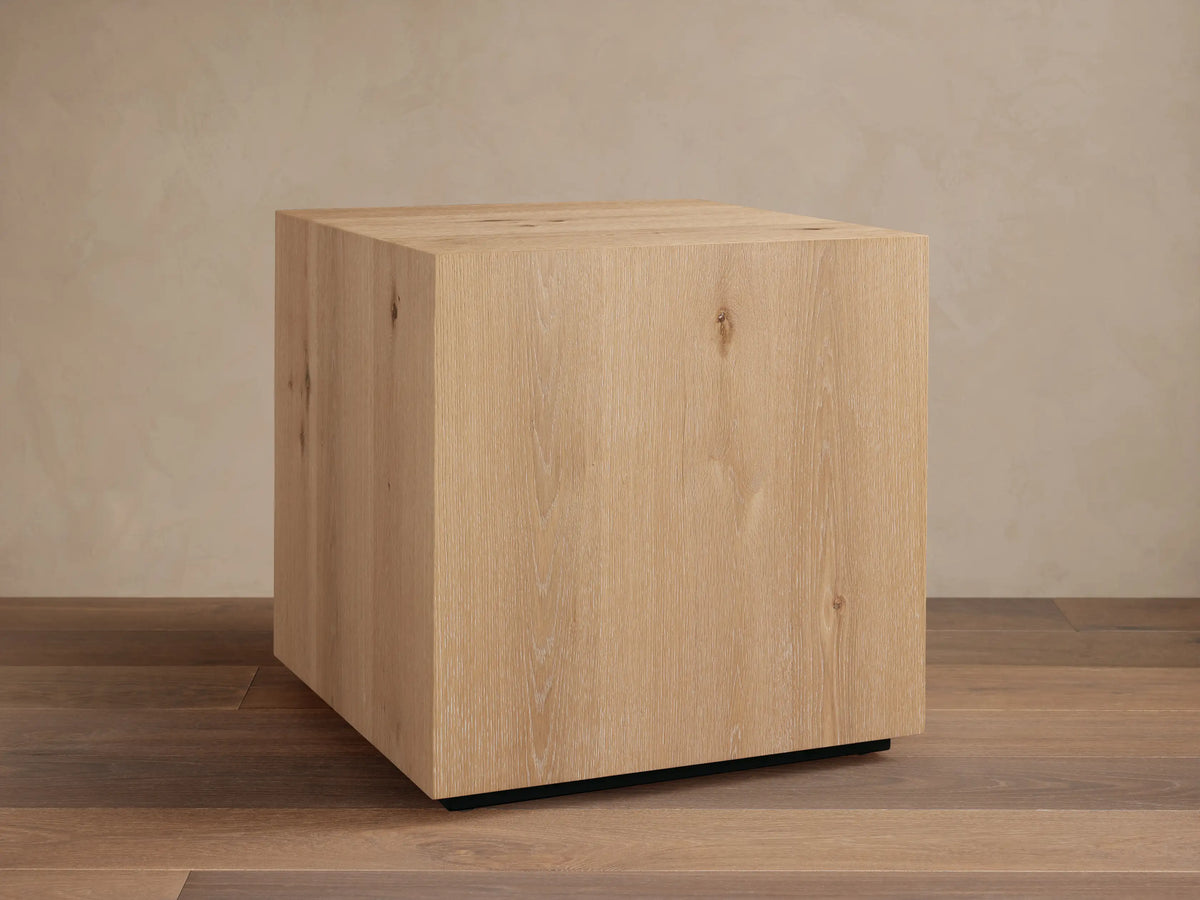 Sullivan End Table made from light oak with visible wood grain, square shape, and black plinth-style base, set on wood floor.