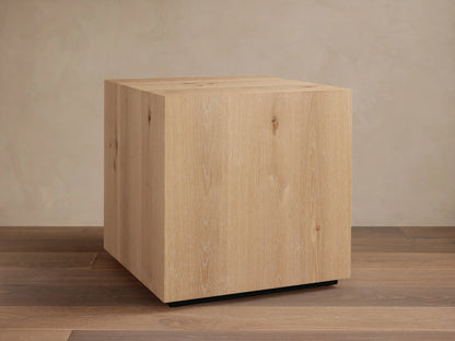 Sullivan End Table made from light oak with visible wood grain, square shape, and black plinth-style base, set on wood floor.