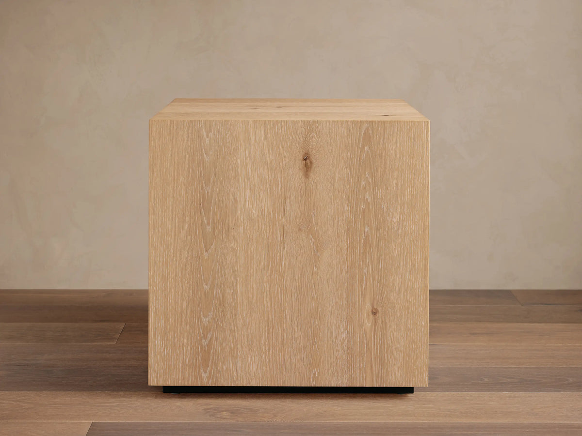 Sullivan End Table made from light oak with visible wood grain, square shape, and black plinth-style base, set on wood floor.