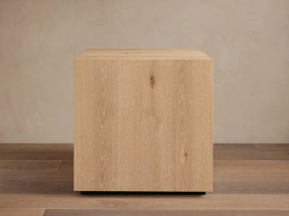 Sullivan End Table made from light oak with visible wood grain, square shape, and black plinth-style base, set on wood floor.