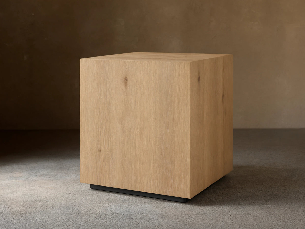Sullivan End Table made from light oak with visible wood grain, square shape, and black plinth-style base, set on wood floor.