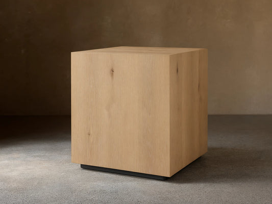 Sullivan End Table made from light oak with visible wood grain, square shape, and black plinth-style base, set on wood floor.
