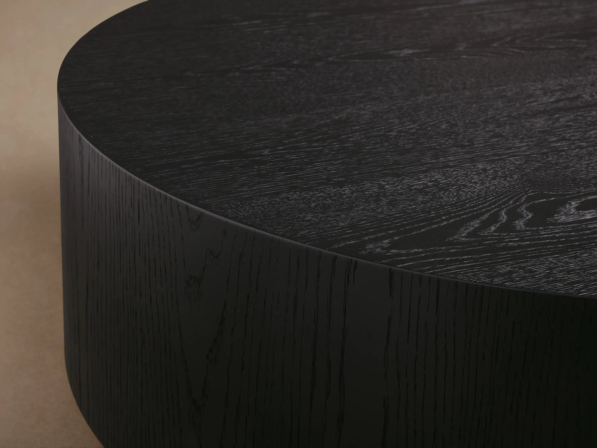 Front view of the natural oak Sullivan Round Coffee Table, showing its round tabletop and black plinth-style base.