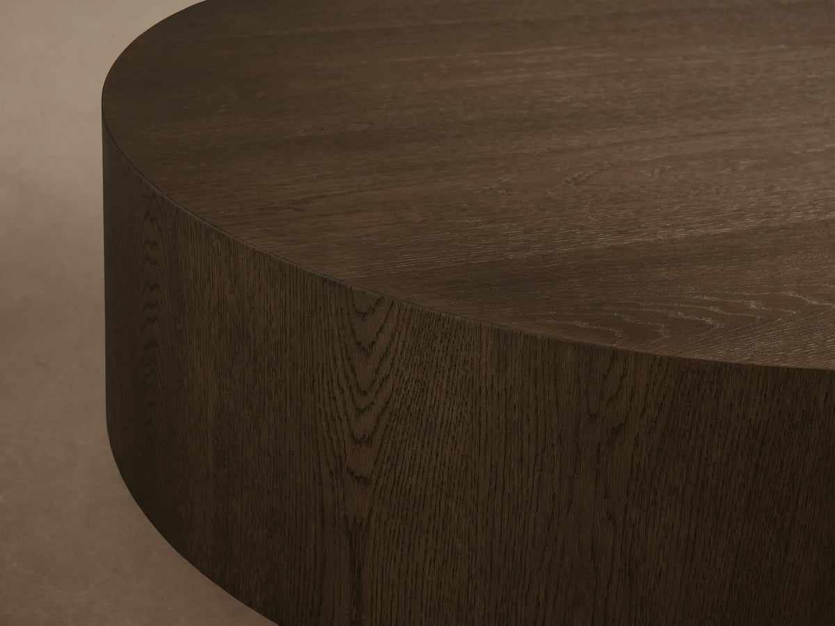Sullivan Round Coffee Table, made of light oak wood with a black base, showcasing an open book and white vase on top.