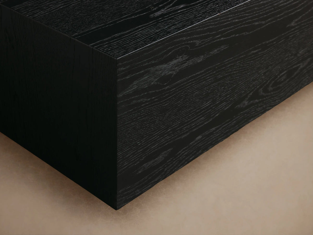 Sullivan Coffee Table with a rectangular black finish, solid oak construction, resting on a plinth-style base, on a wooden floor.