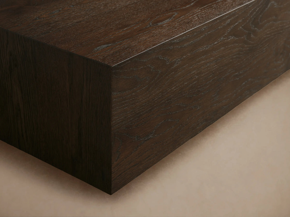 Sullivan Coffee Table made of dark solid oak with visible natural wood grain, rectangular shape on a black plinth base, in a minimal setting.