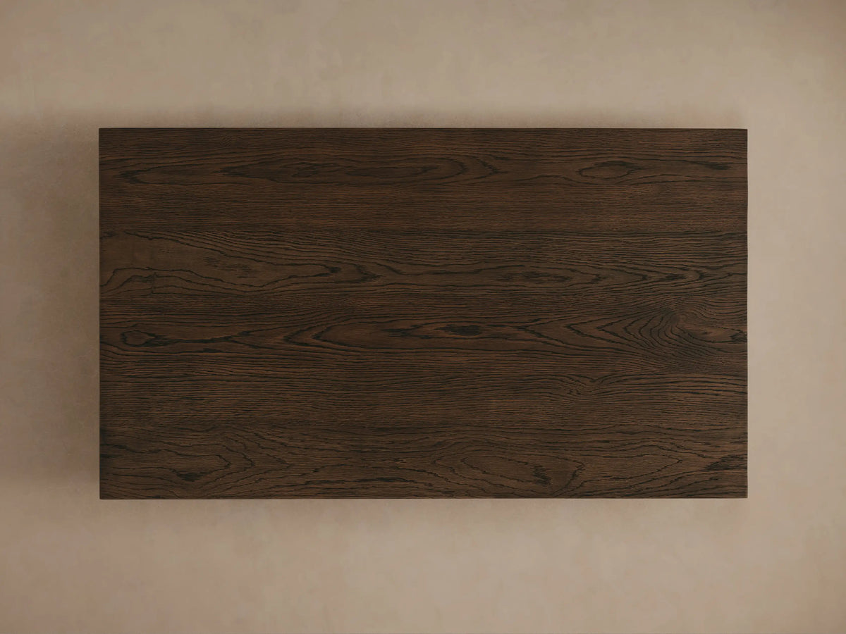 Dark brown Sullivan Coffee Table with visible wood grains and texture, corner view showing black plinth-style base on a light surface.