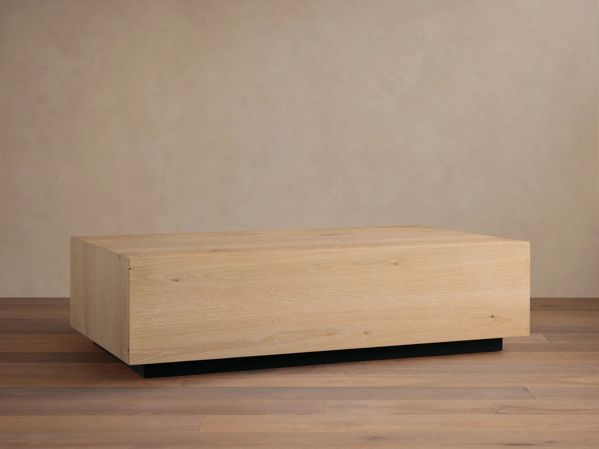 Sullivan Coffee Table with a rectangular European oak surface, showing weathered texture, atop a black plinth base on wood flooring.