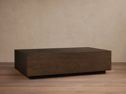 Sullivan Coffee Table features a rectangular, dark oak tabletop with a natural grain pattern, resting on a black plinth-style base.