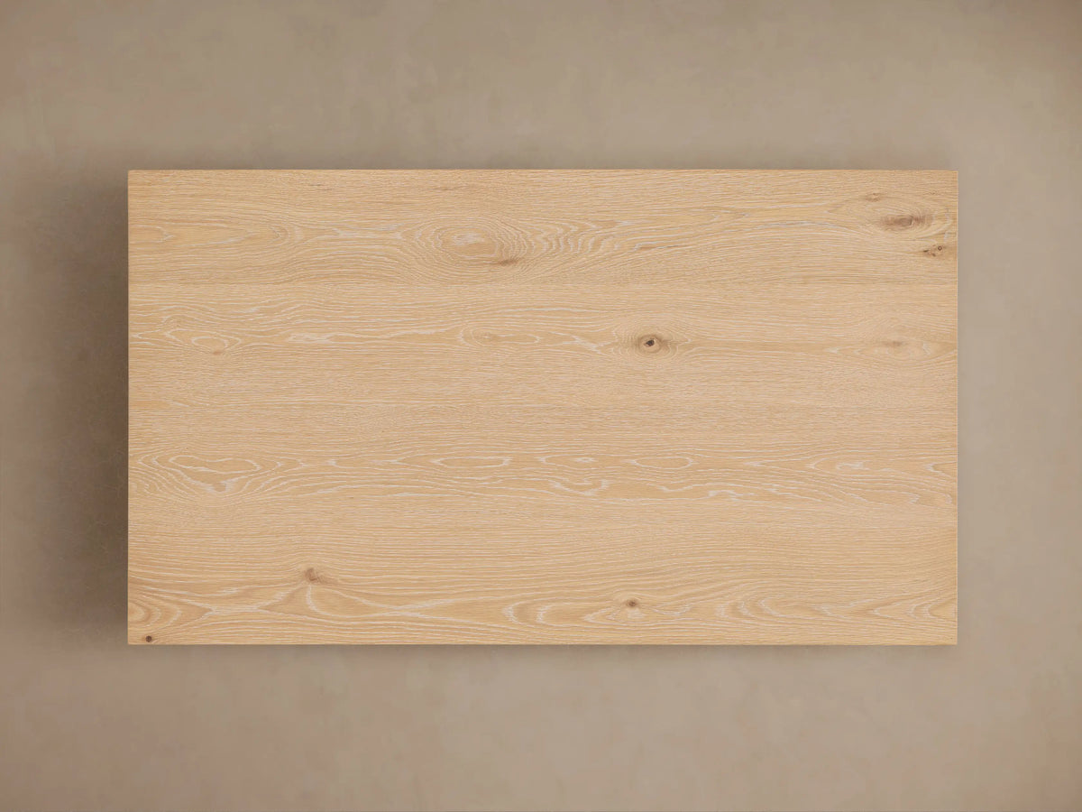 Sullivan Coffee Table corner view in solid oak with visible wood grain, resting on a black plinth-style base, showing natural texture.