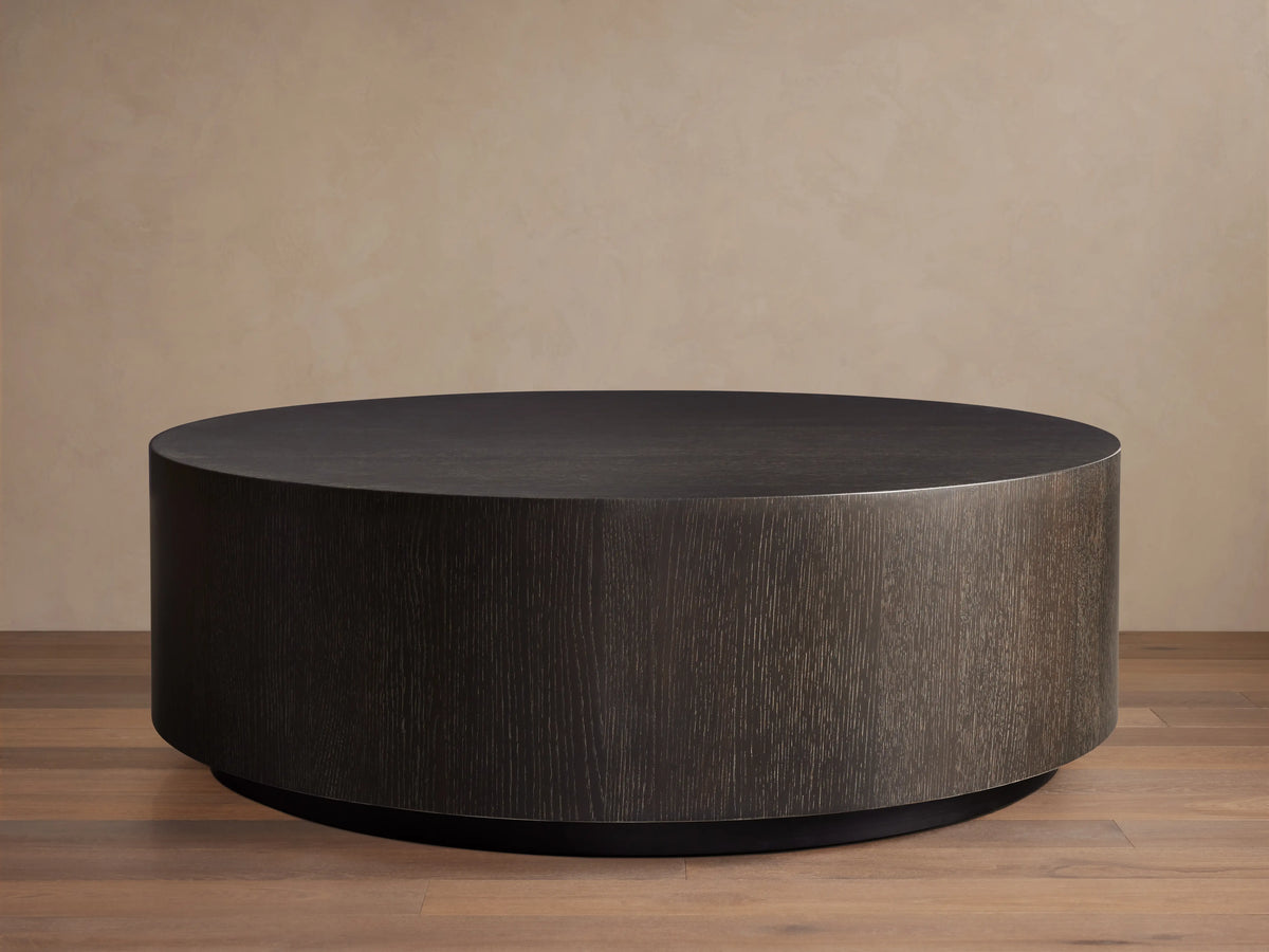 Round wooden coffee table in dark brown Northman Cinder finish, showcasing a smooth top and grained sides on wooden floor.
