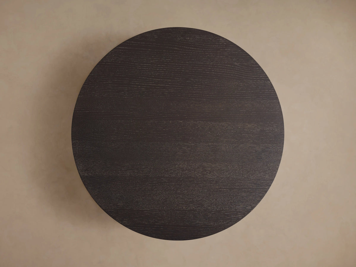 Round coffee table in dark Northman Cinder finish viewed from above, showing the smooth, rich wood grain texture.