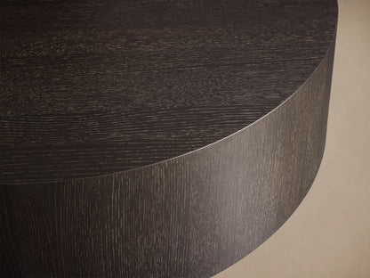 Round wooden coffee table in dark brown Northman Cinder finish, showcasing a smooth top and grained sides on wooden floor.