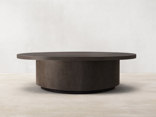 Round wooden coffee table in dark brown Northman Cinder finish, showcasing a smooth top and grained sides on wooden floor.