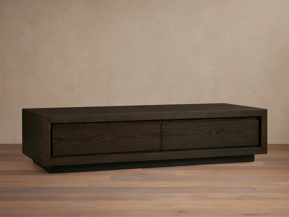 Sullivan Storage Coffee Table in dark oak finish with a rectangular form. It has two soft-close drawers and rests on a black plinth base.