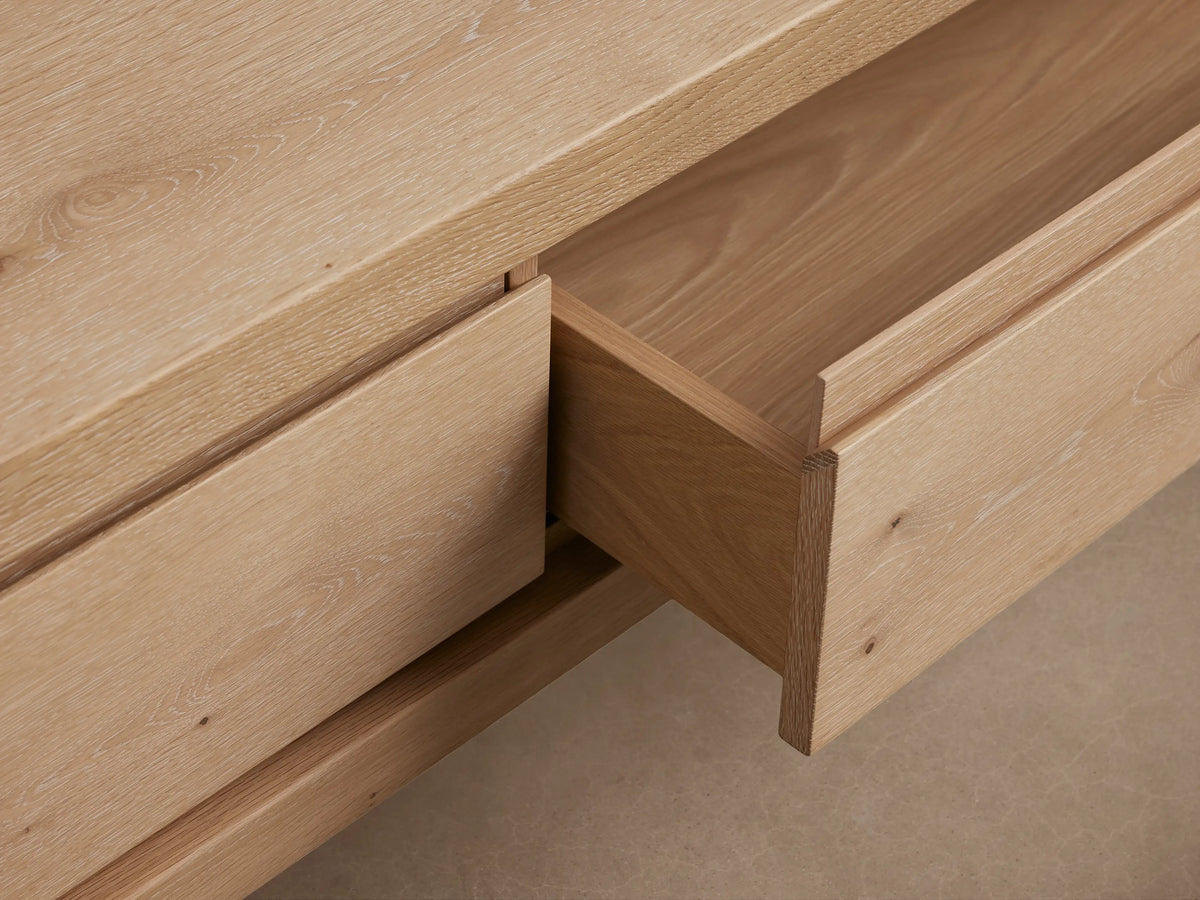 Sullivan Storage Coffee Table made of light European oak wood with natural cracks and knots, featuring two drawers and a black plinth-style base.