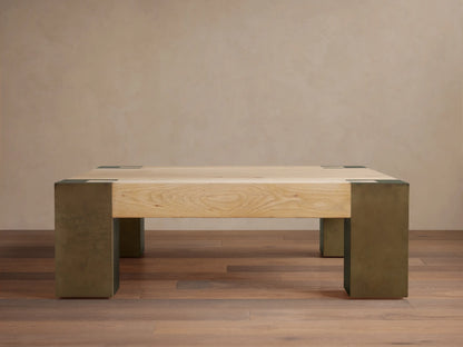 Light oak square Telluride coffee table with four legs of oxidized steel with dark patinas, against a beige wall and wood floor.