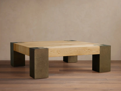 Light oak square Telluride coffee table with four legs of oxidized steel with dark patinas, against a beige wall and wood floor.