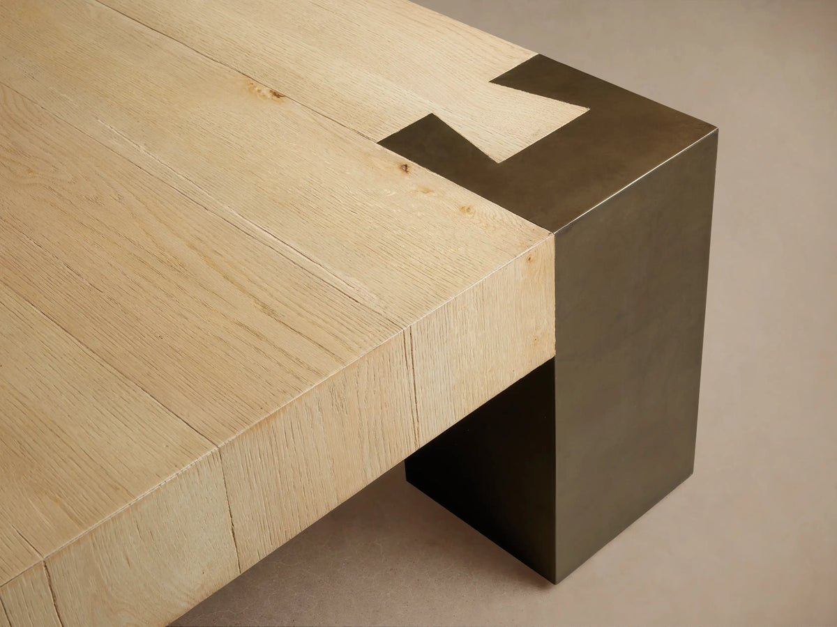 Telluride Square Coffee Table with a light oak wood top and dark, weathered steel corner legs. On a wooden floor.