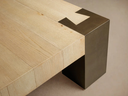 Telluride Square Coffee Table with a light oak wood top and dark, weathered steel corner legs. On a wooden floor.