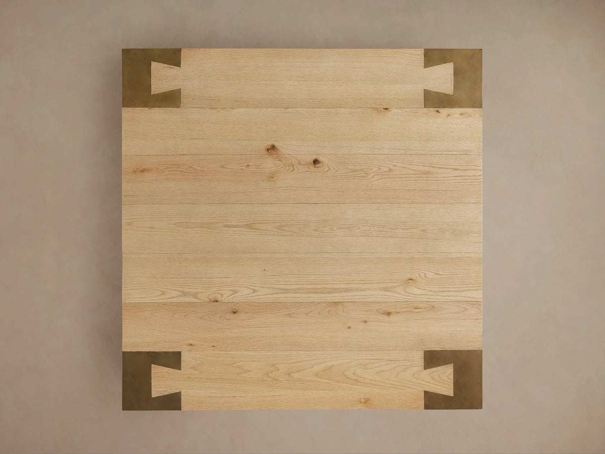 Close-up of a Telluride Square Coffee Table, featuring a light oak wood top with grain details and a dark oxidized steel leg.