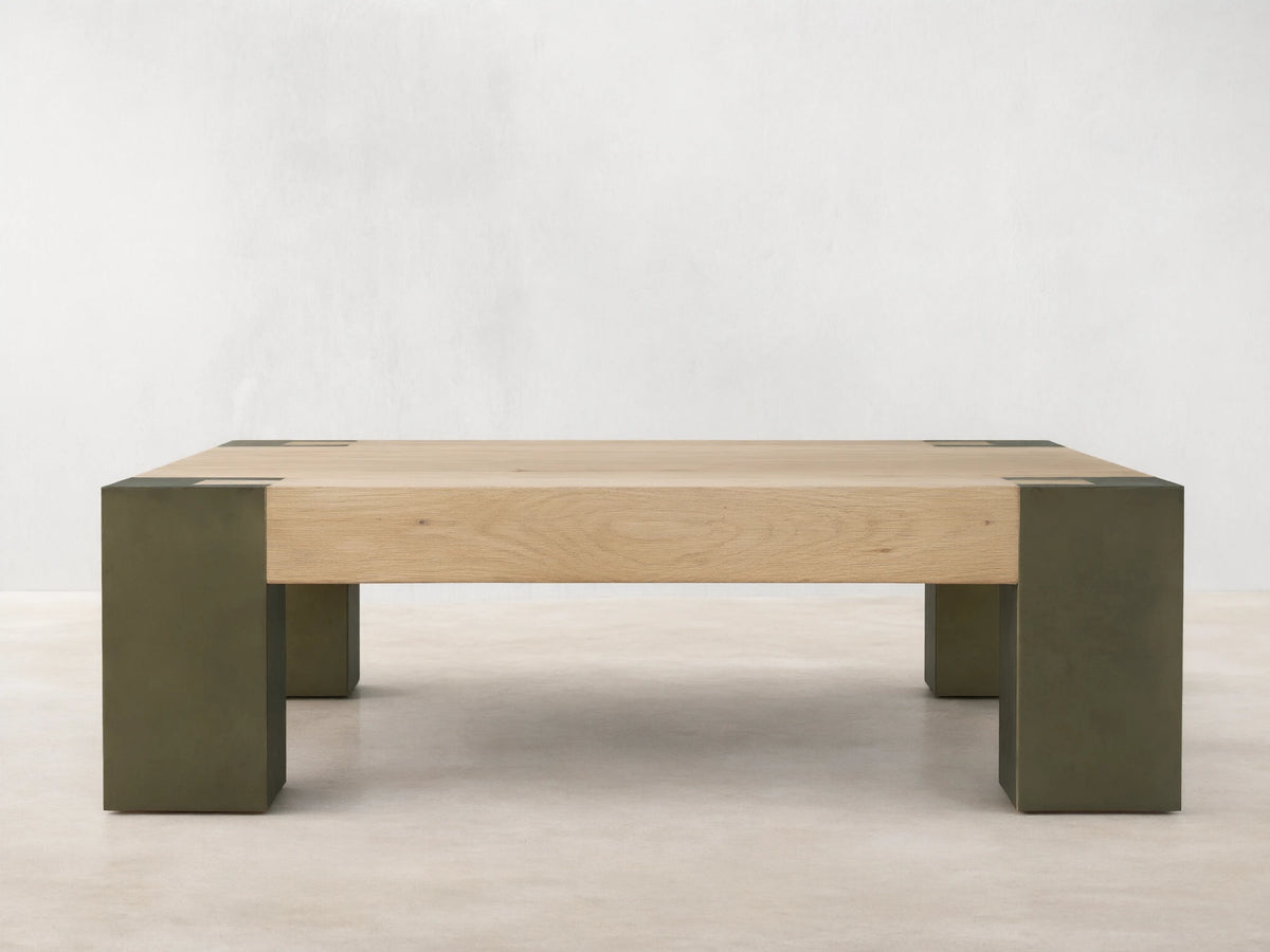 Light oak square Telluride coffee table with four legs of oxidized steel with dark patinas, against a beige wall and wood floor.