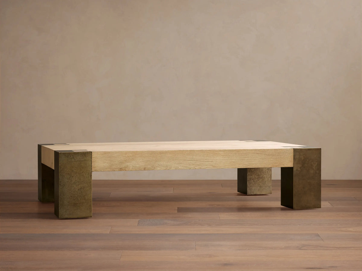 Telluride Coffee Table, light oak veneer top with visible grain, naturally oxidized steel legs & corner accents, on a wood floor.