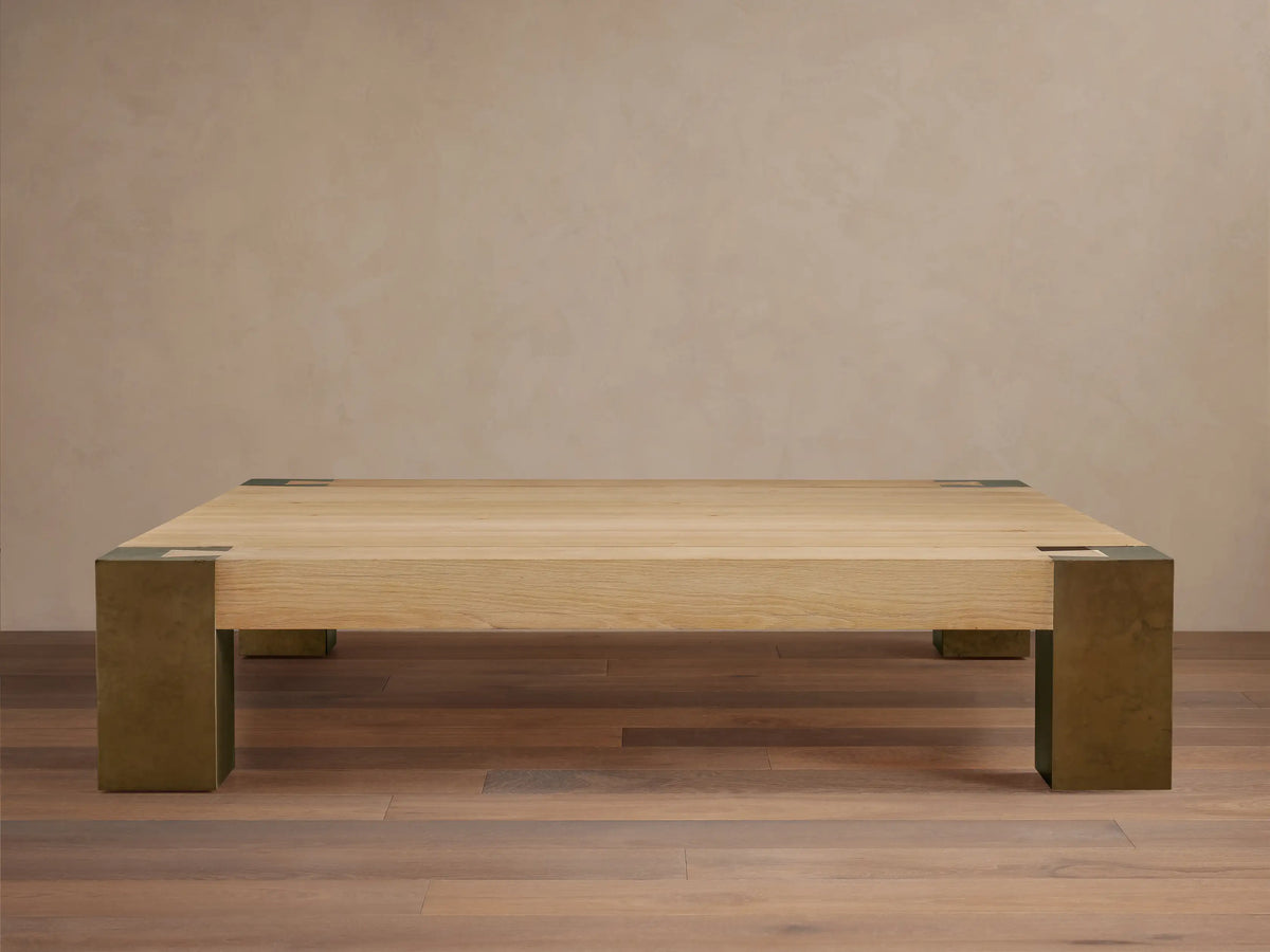 Telluride Square Coffee Table with light oak veneer top & thick, dark oxidized steel corner legs. On wood floor against a light wall.
