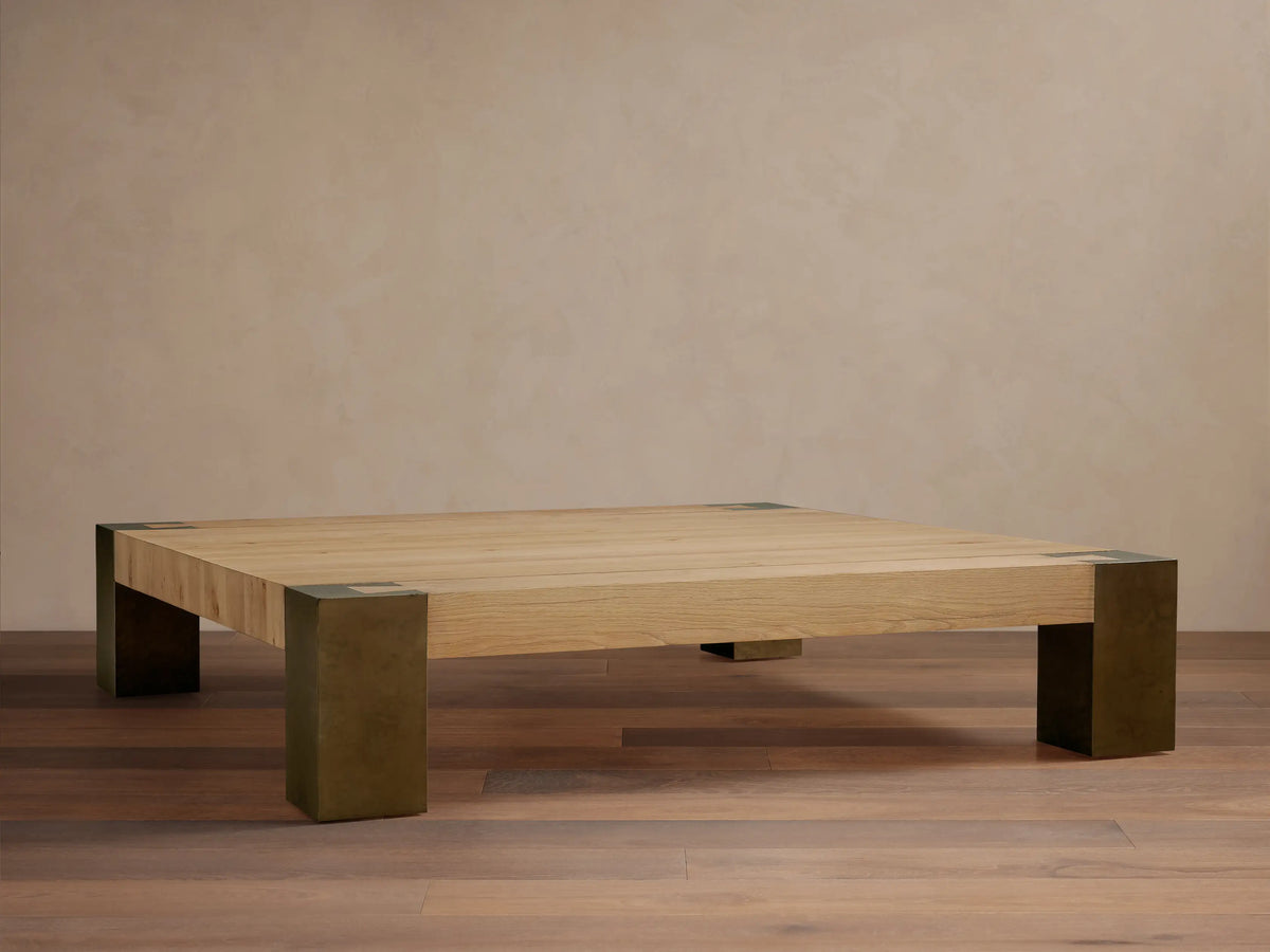 Telluride Square Coffee Table with light oak veneer top & thick, dark oxidized steel corner legs. On wood floor against a light wall.
