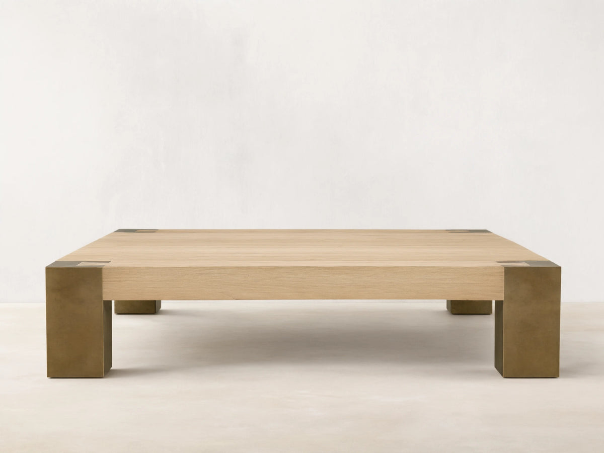 Telluride Square Coffee Table with light oak veneer top & thick, dark oxidized steel corner legs. On wood floor against a light wall.