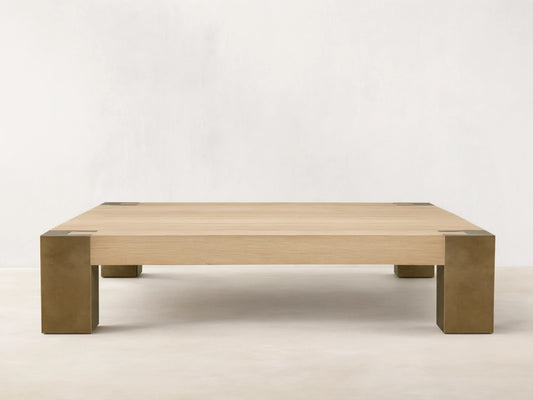 Telluride Square Coffee Table with light oak veneer top & thick, dark oxidized steel corner legs. On wood floor against a light wall.