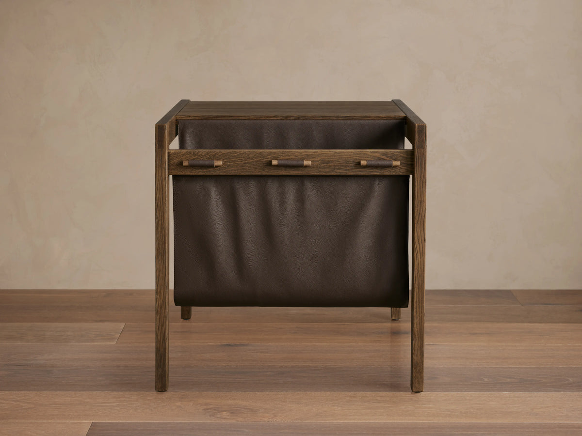 Thorin Magazine Table made of solid oak with a hand-applied finish. Features a dark leather sling on the side for storage.