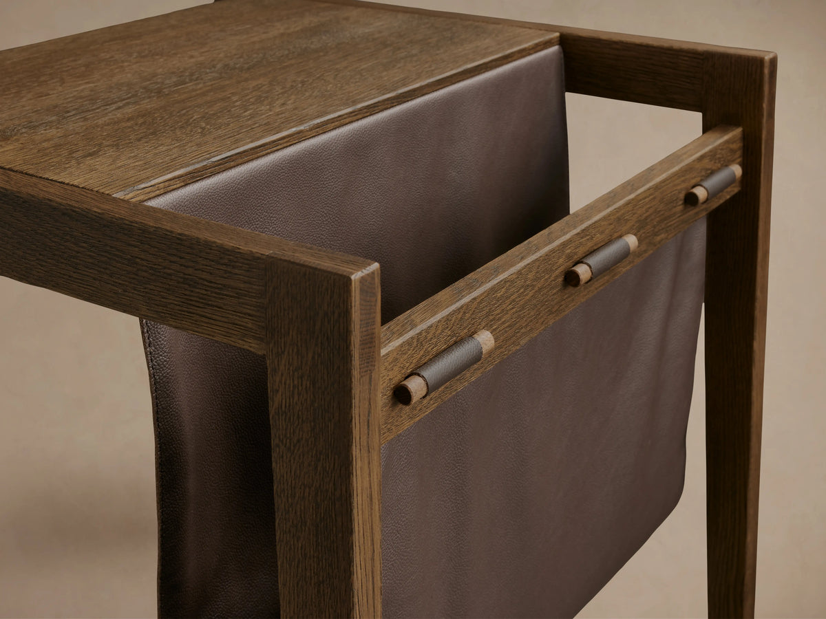 Thorin Magazine Table made of solid oak wood with a visible leather sling, supported by wooden dowels, on a wooden floor.