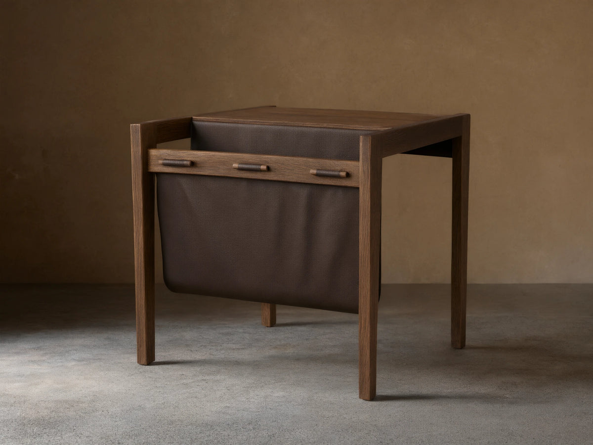 Thorin Magazine Table made of solid oak with a hand-applied finish. Features a dark leather sling on the side for storage.