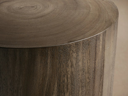 Toluca End Table with a cylindrical shape, dark wood finish, and smooth surface, placed on wooden floor against a light wall.