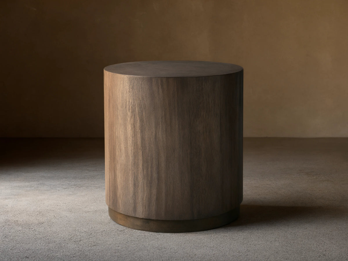 Toluca End Table with a cylindrical shape, dark wood finish, and smooth surface, placed on wooden floor against a light wall.