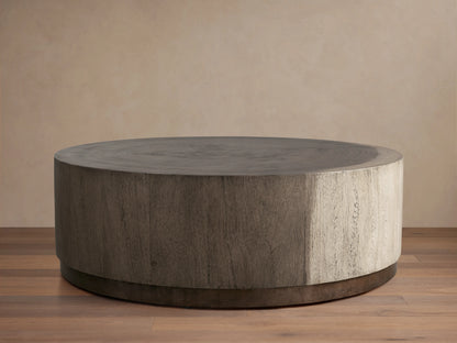 Round Toluca Coffee Table, weathered grey guanacaste wood grain top & sides, dark oxidized metal base on wood floor.