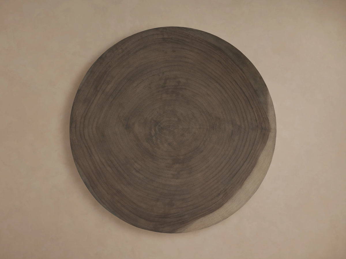 Toluca Coffee Table: Round, dark brown guanacaste wood tabletop, showing prominent tree rings, against a light beige wall.