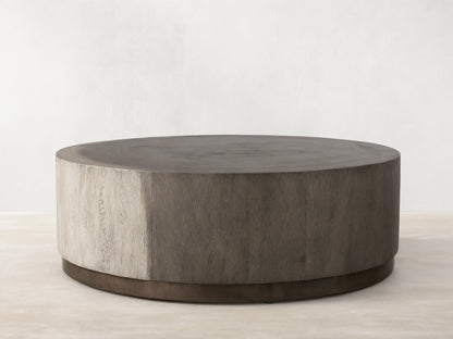 Round Toluca Coffee Table, weathered grey guanacaste wood grain top & sides, dark oxidized metal base on wood floor.