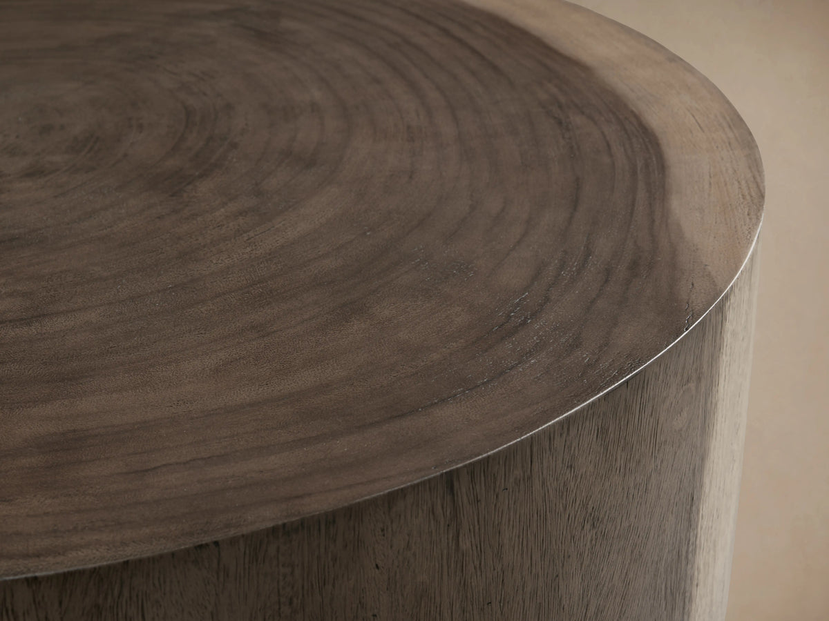Round Toluca Coffee Table, weathered grey guanacaste wood grain top & sides, dark oxidized metal base on wood floor.