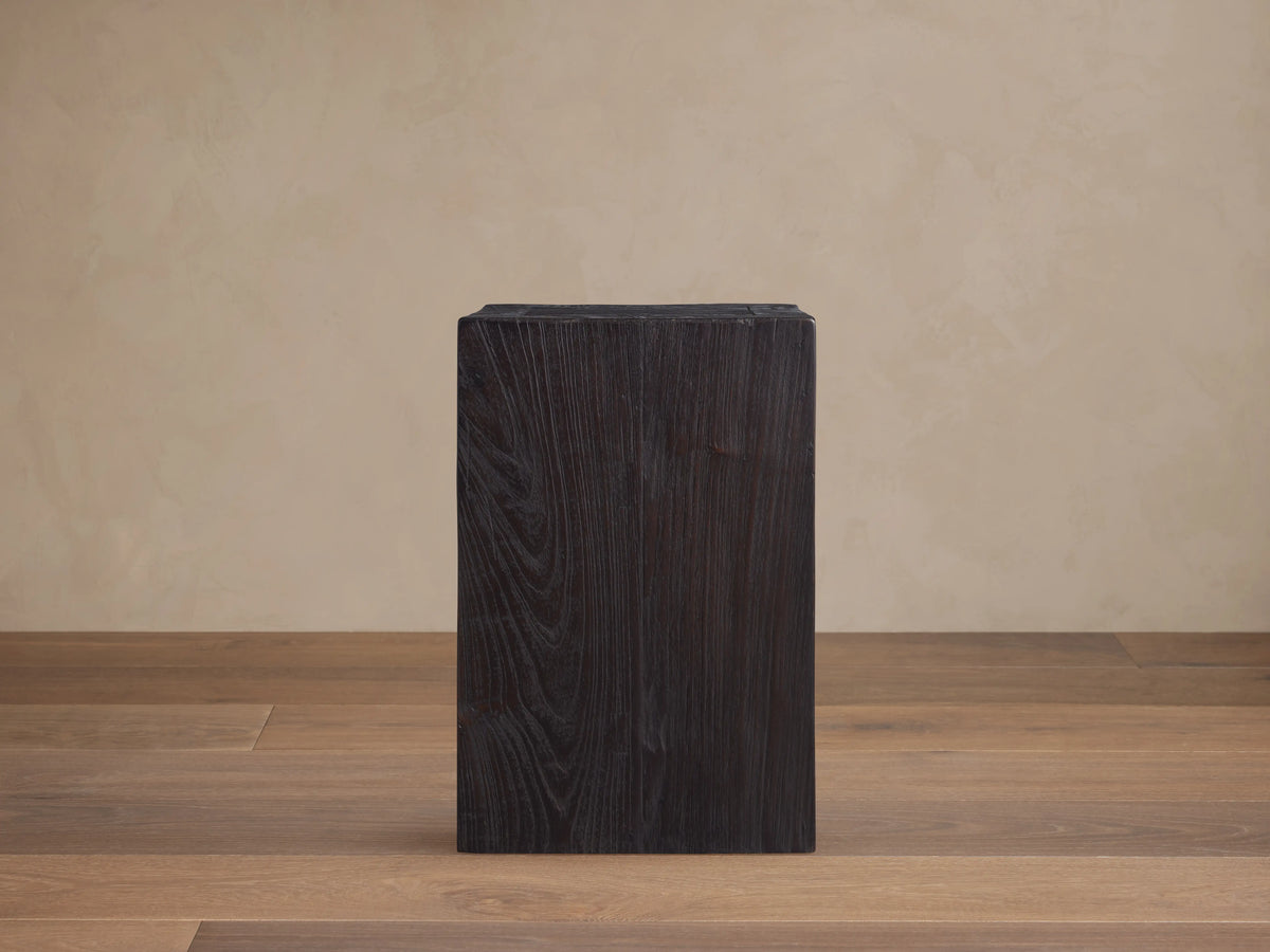 A dark, rectangular Ubud Pedestal made from reclaimed teak wood with a rich black, textured Shou Sugi Ban finish, on wooden floor.