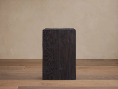 A dark, rectangular Ubud Pedestal made from reclaimed teak wood with a rich black, textured Shou Sugi Ban finish, on wooden floor.