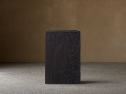 A dark, rectangular Ubud Pedestal made from reclaimed teak wood with a rich black, textured Shou Sugi Ban finish, on wooden floor.
