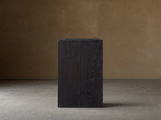A dark, rectangular Ubud Pedestal made from reclaimed teak wood with a rich black, textured Shou Sugi Ban finish, on wooden floor.