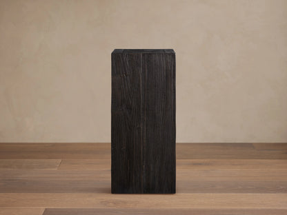 Tall, rectangular Ubud Pedestal made of teak wood with a dark, charred finish and visible grain patterns, set on a wooden floor background.