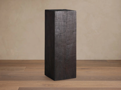 Ubud Pedestal crafted from dark reclaimed teak wood with a textured, charred finish. Tall, rectangular shape on a wooden floor.