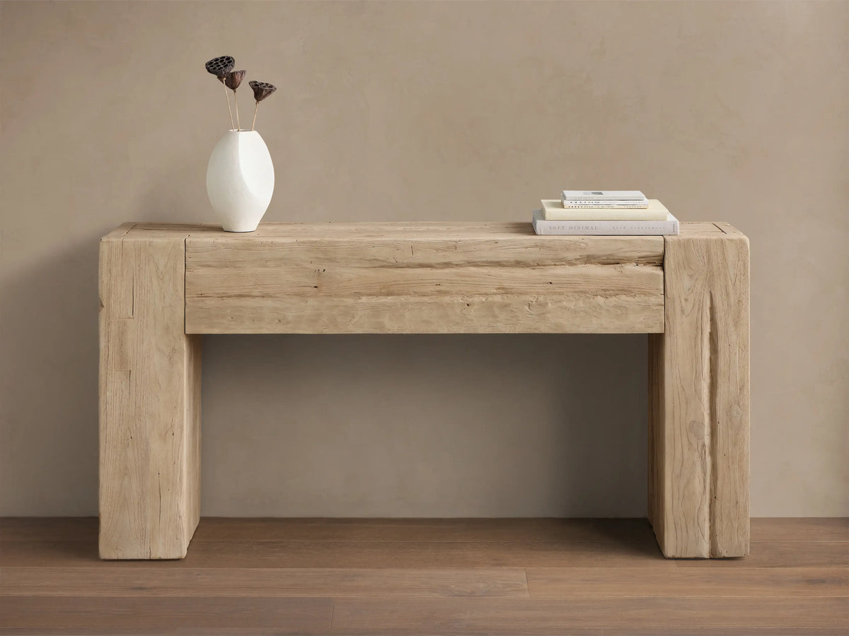 Front view of the Driftwood Ubud Console Table, a rustic reclaimed teak wood table with thick block legs, adorned with a white vase and books.