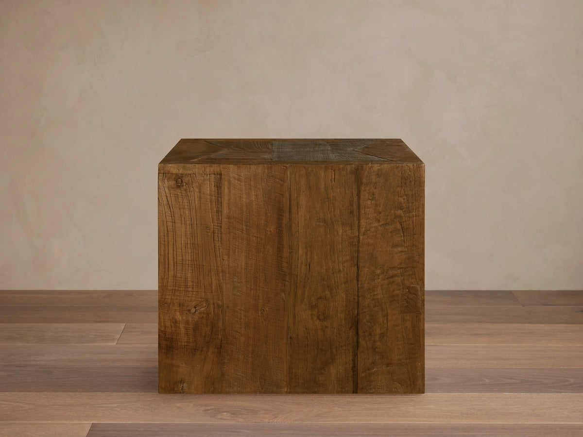 Ubud End Table made from reclaimed teak wood in a cube shape. Natural brown finish with visible grain and knots on a wooden floor.